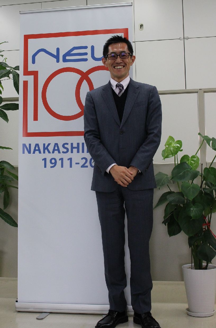創立100周年記念のパネルの前で中島田社長
